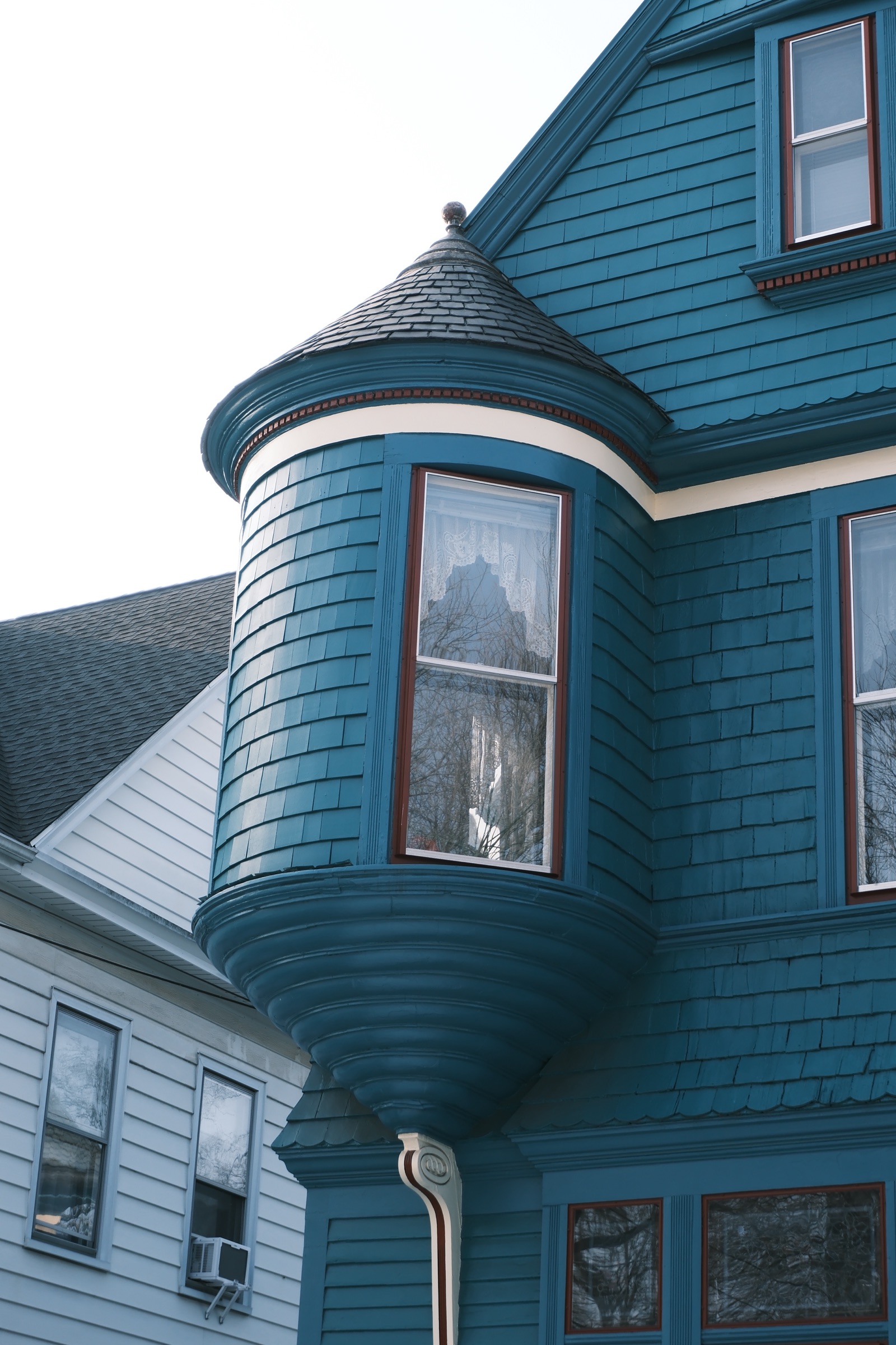 A teal Victorian house with a rounded turret and bay window, its panes reflecting bare trees