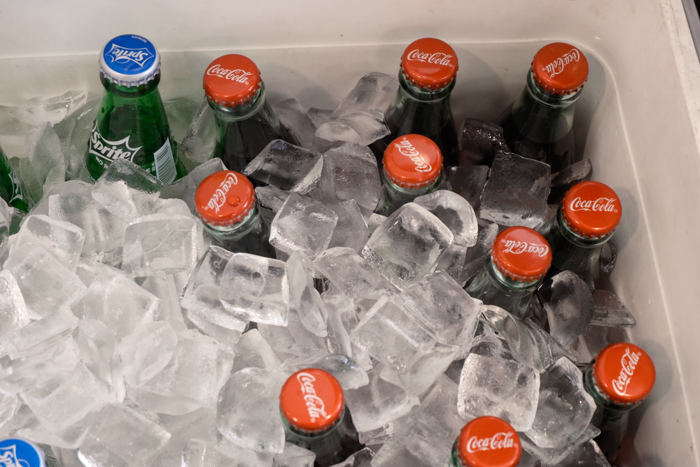 Glass Coca-Cola and Sprite bottles packed upright in a cooler of ice